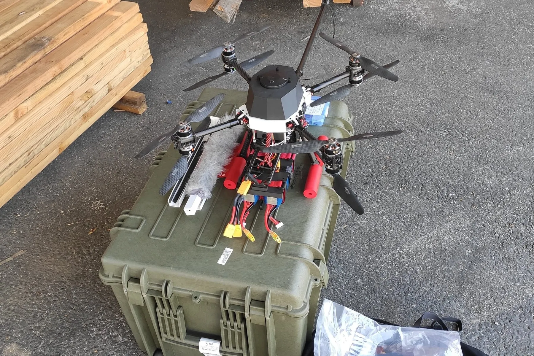 Coaxial quadcopter assembled on top of its closed Pelican case, stacked timber and a kit backpack around it.