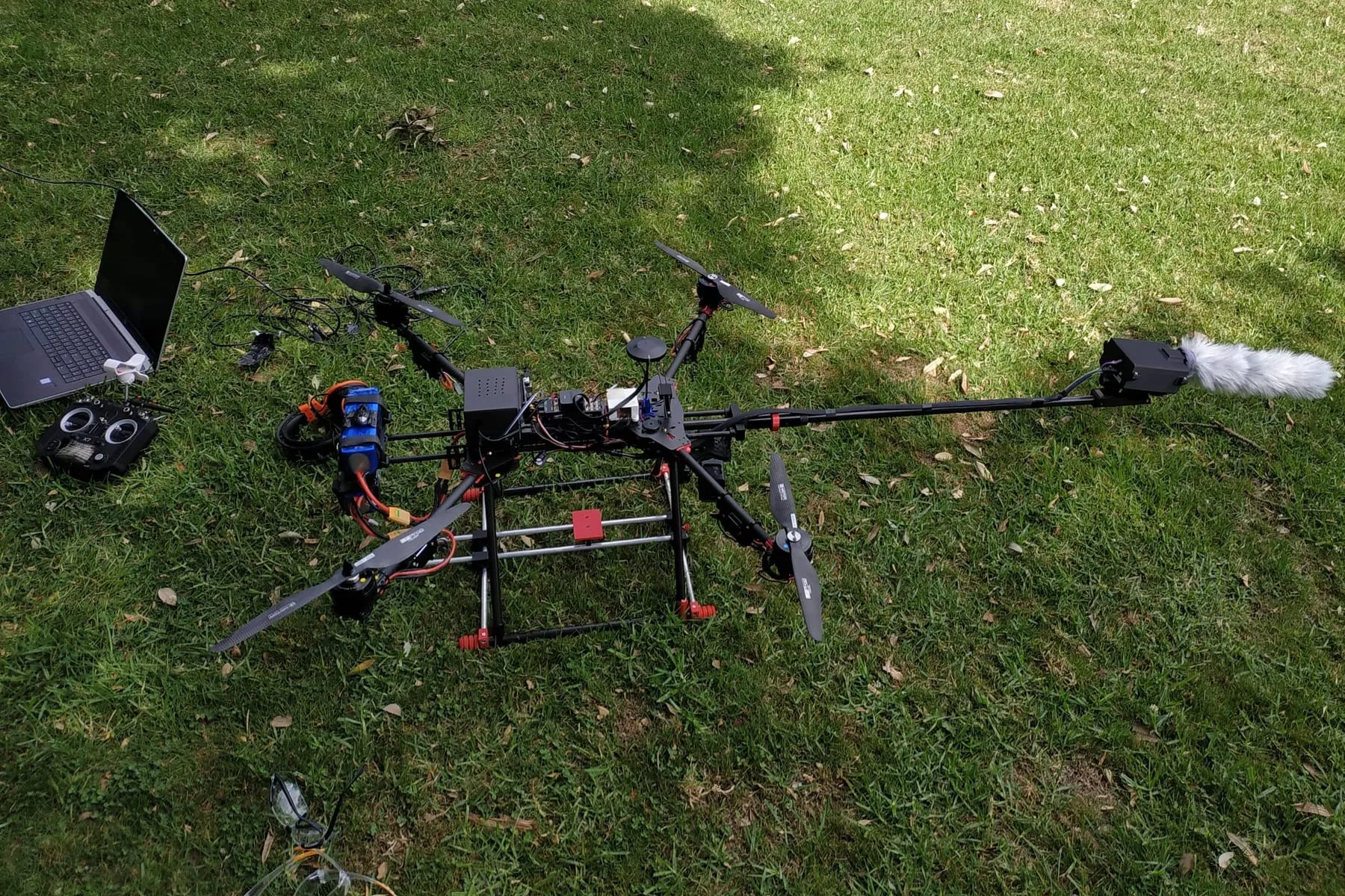 Skylark M4-680 on grass with a microphone on a forward boom in a fur windshield, a laptop and a transmitter laid out beside it.