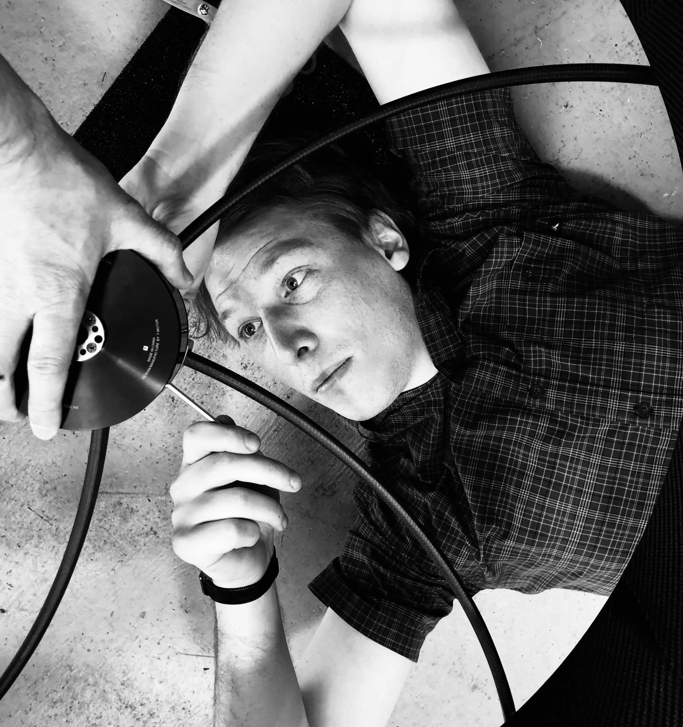 Lying beneath a 32-inch acoustic shroud, driving a fastener into its motor mount while a colleague steadies the motor.